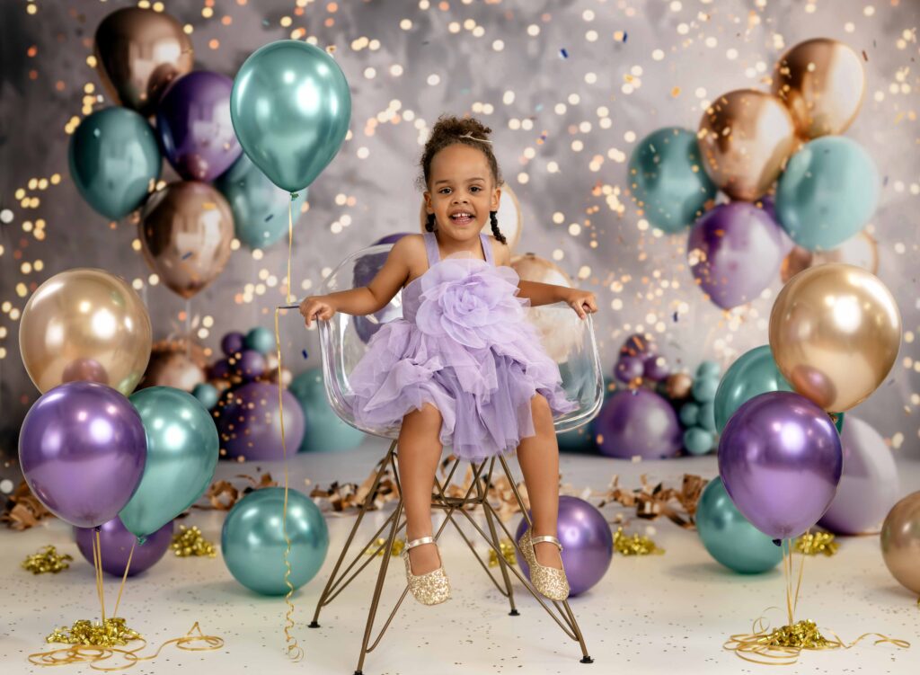 3 year toddler taking birthday photos at Atlanta photo studio with teal and gold and lavender balloons.