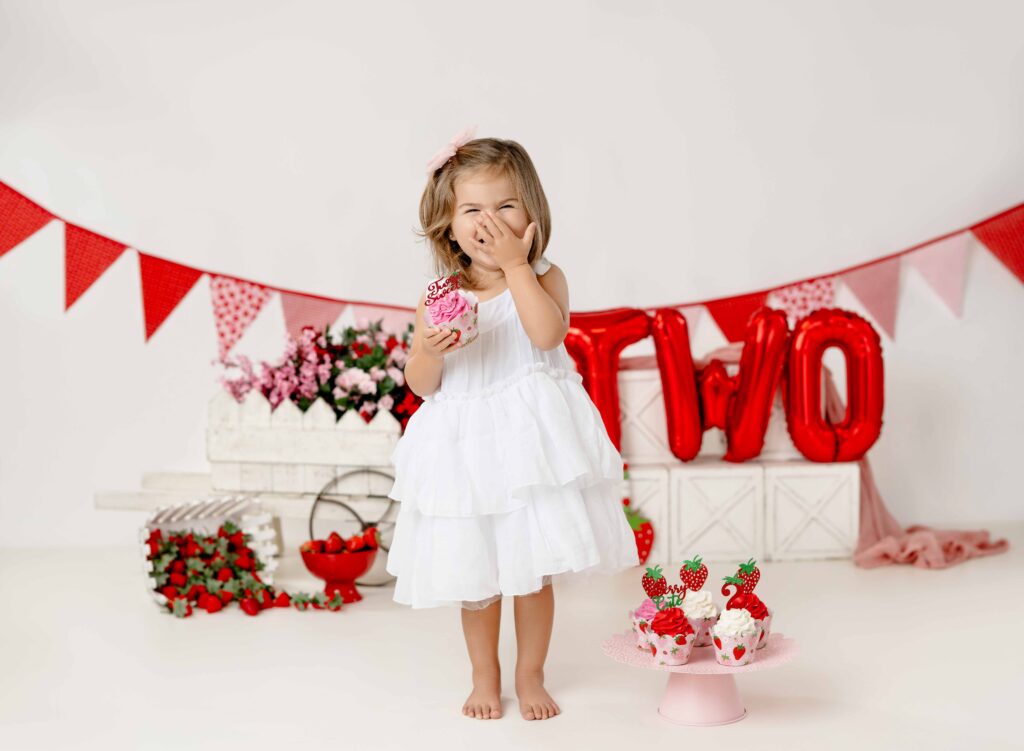 2 year old girl in white dress laughing with hand over mouth.