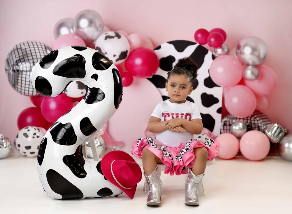 2 year old girl sitting on bench in front of disco cowgirl birthday set.