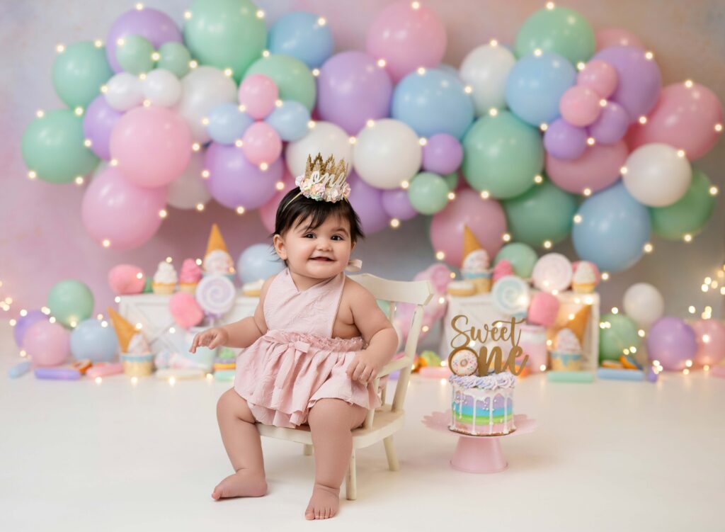 Baby girl in chair smiling in front of a birthday cake smash set.