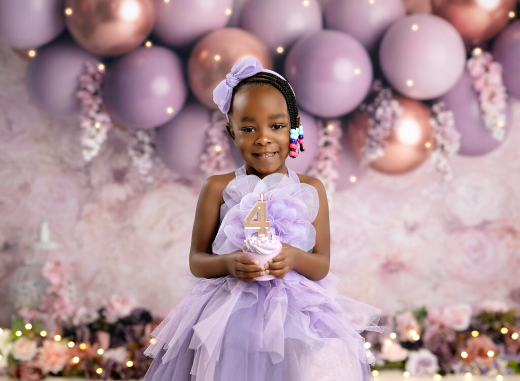 toddler holding cupcake and smiling for 4th birthday session.