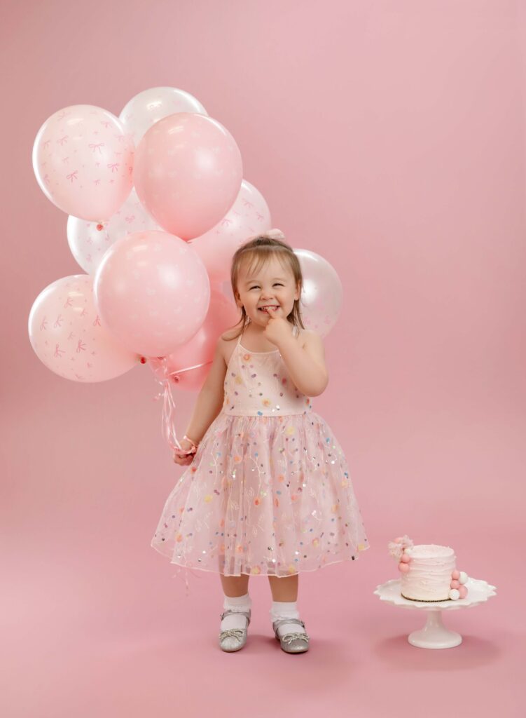 Toddler girl holding balloons and giggling.