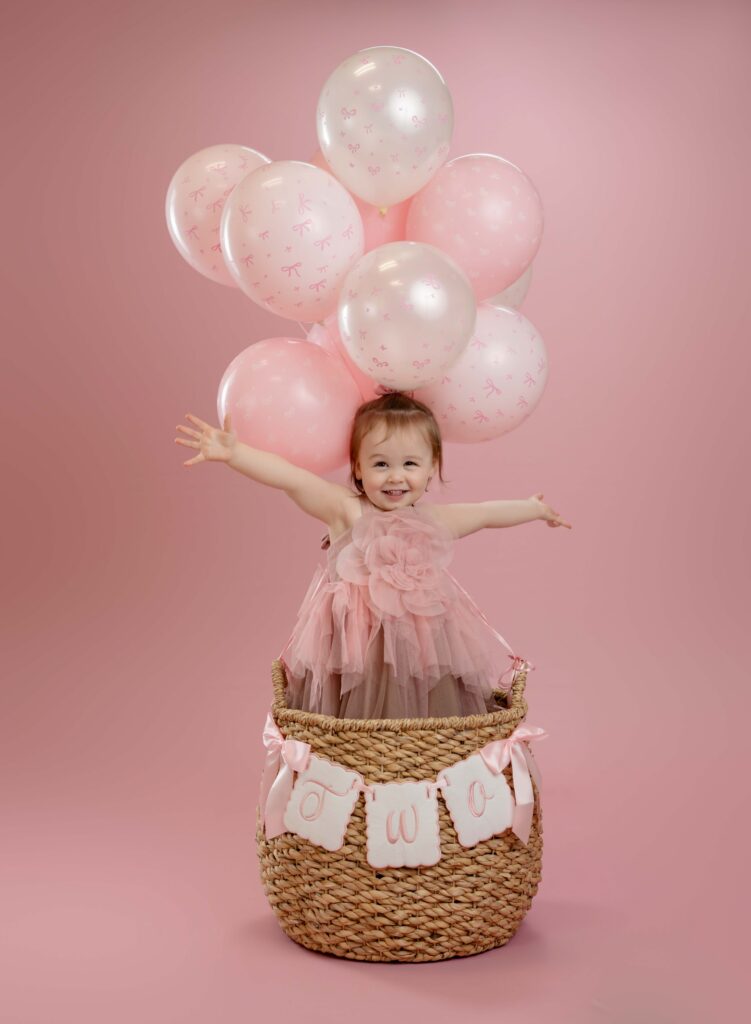 Toddler girl in balloon basket with arms wide open and smiling.