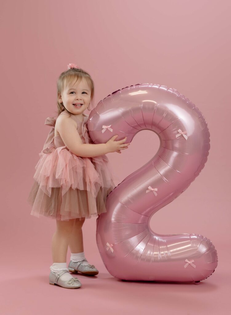 Toddler holding #1 pink balloon and smiling.