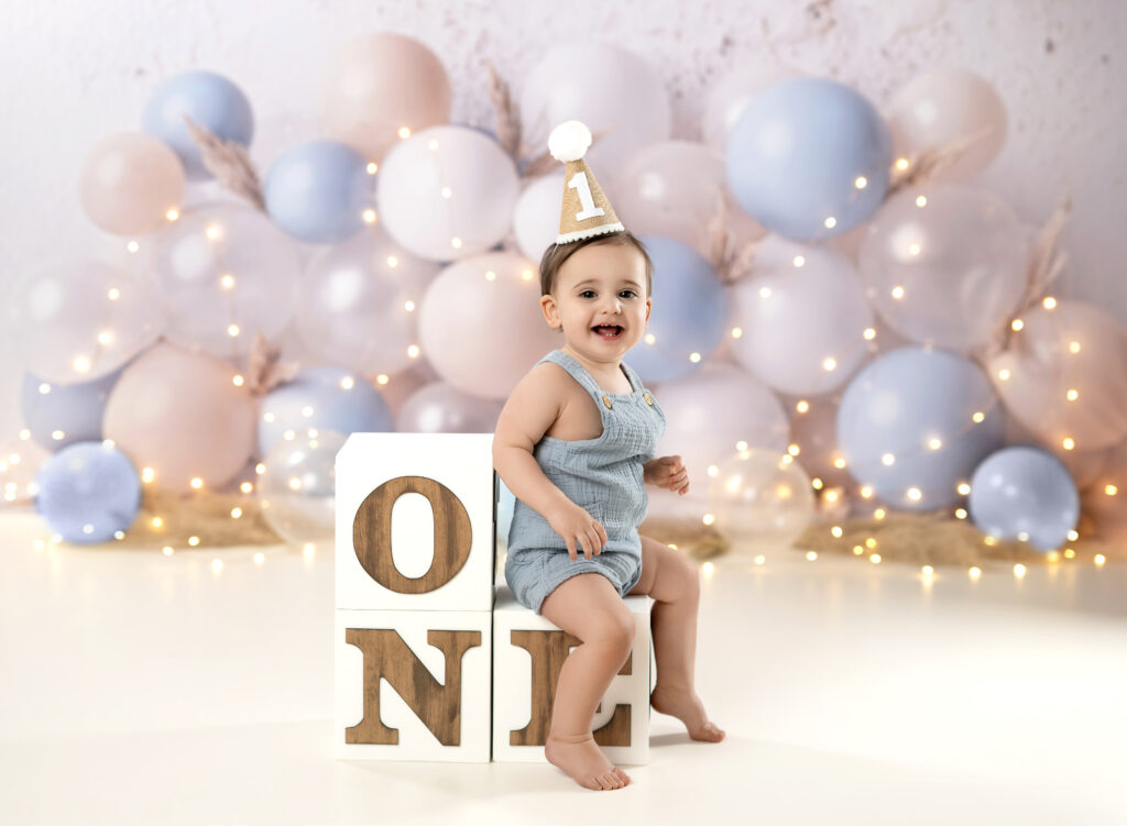 Baby boy sitting on ONE blocks and taking birthday photos smiling.