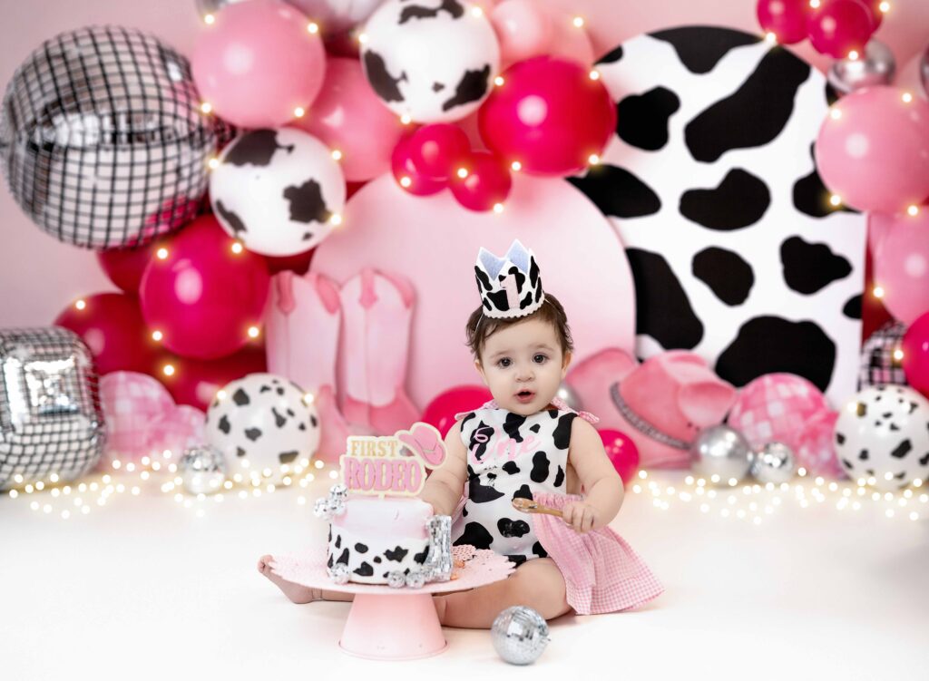 Baby girl in cow print romper eating birthday cake.