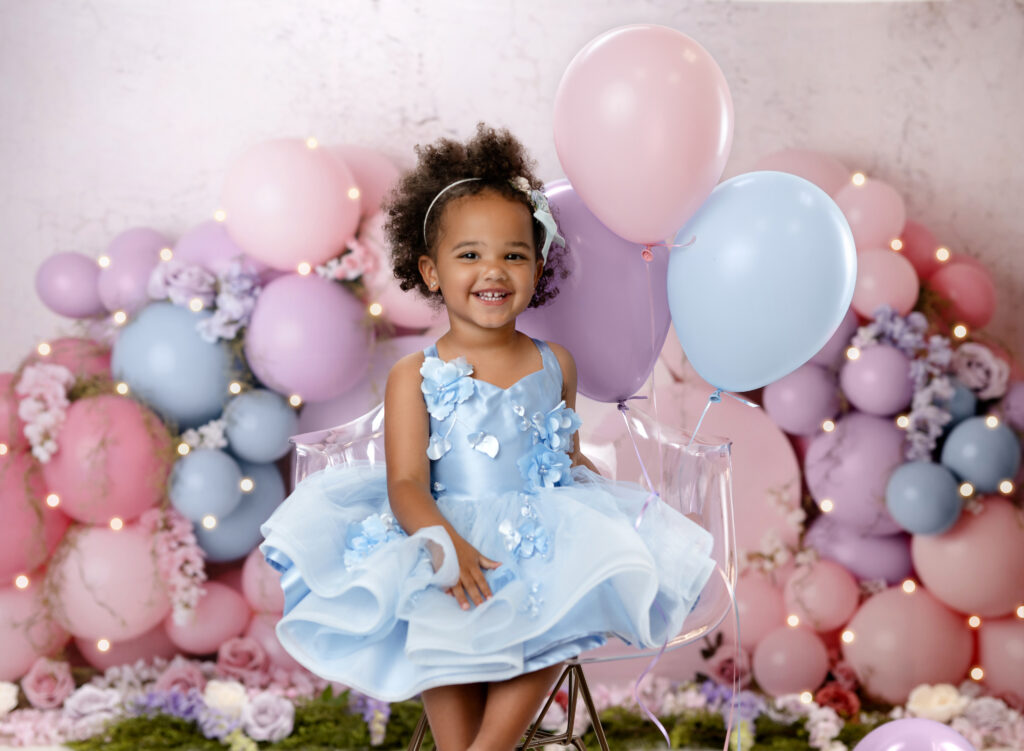 Birthday girl sitting in chair and holding balloons, smiling for her photoshoot.