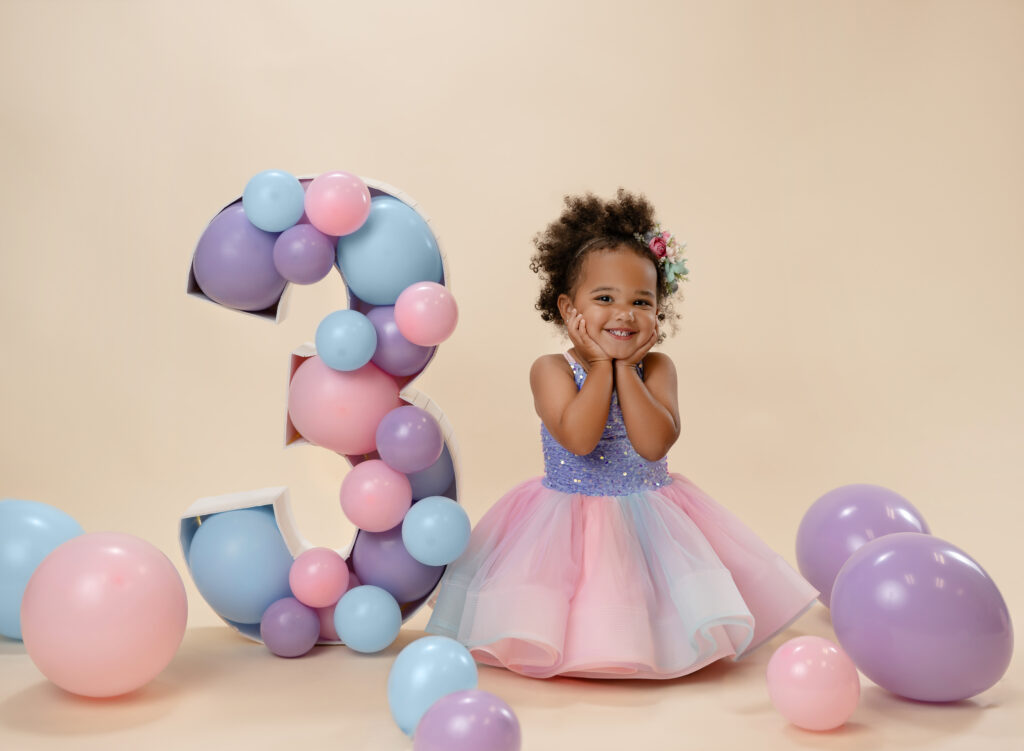 Girl on knees with pastel dress, with her hands under her chin smiling for her birthday photo. 