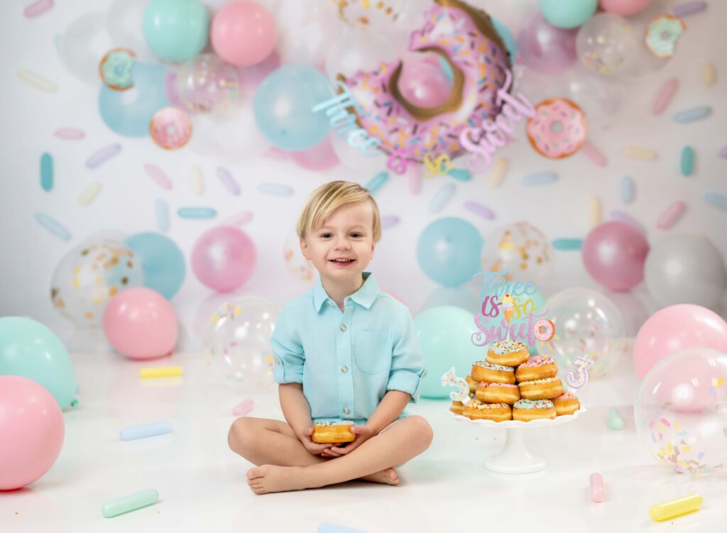 Toddler boy smiling and eating a donut for his 3rd birthday photos.
