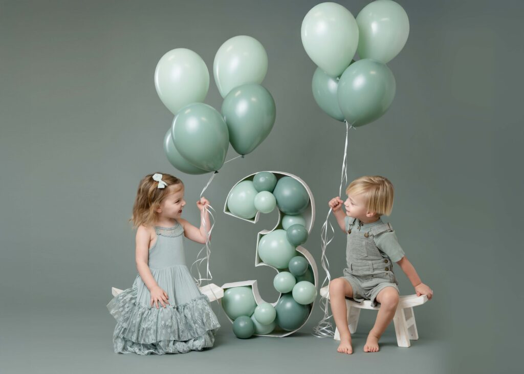 Twins holding balloons and smiling at each other.