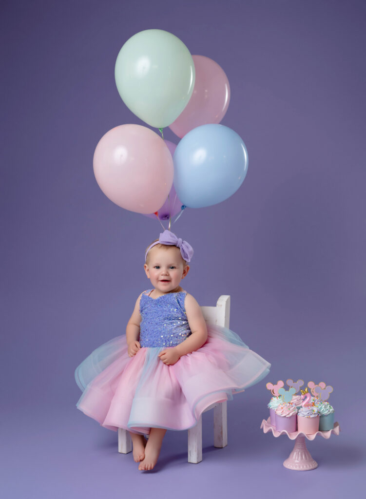 Girl in chair with pastel balloons and smiling at camera