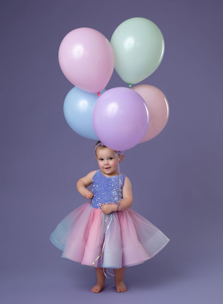 Little girl holding balloons and smiling.