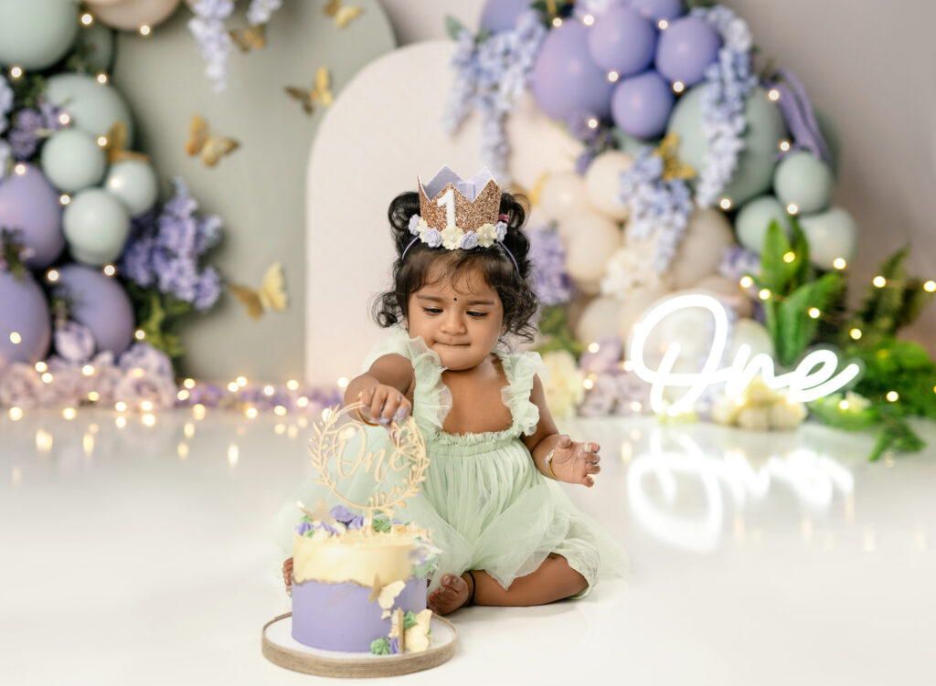 Baby girl in mint green dress, touching her first birthday cake.