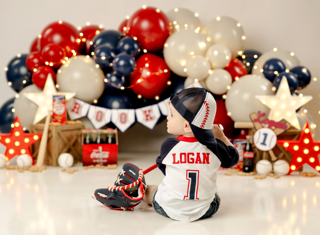 Baby's 1st birthday photoshoot- Rookie of the year. Baby is wearing a personalized rookie shirt with a baseball hat and bat.