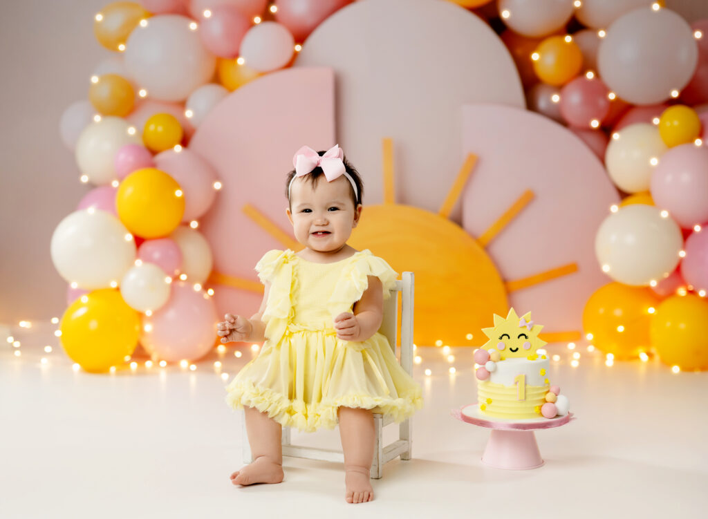 baby girl in yellow dress smiling for her birthday photoshoot.