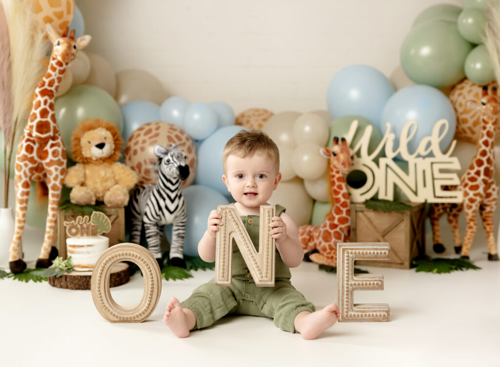 baby boy holding ONE letters in front of a boho safari cake smash birthday set.