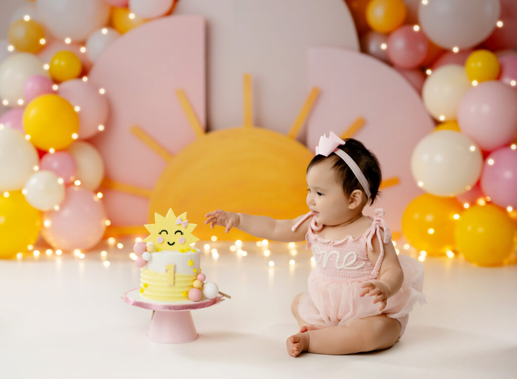 Baby girl taking cake smash photos on a "you are my sunshine" set.