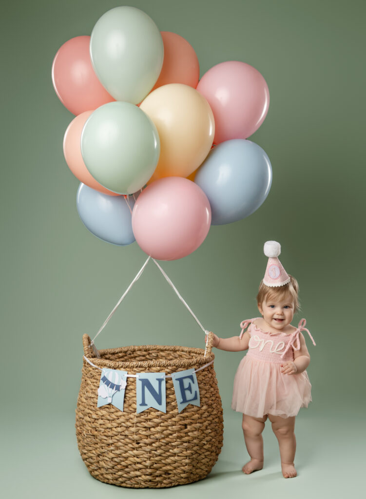 Baby standing by balloon basket taking 1st birthday photos in Aatlanta GA.