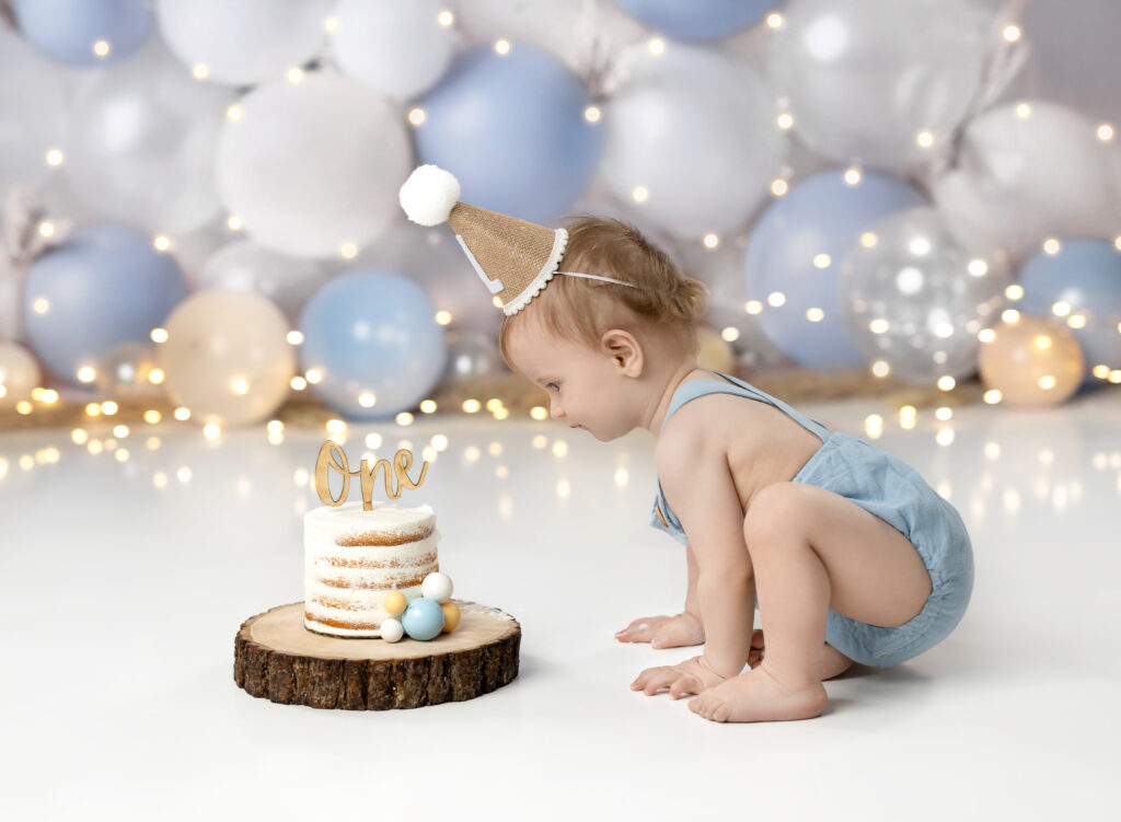 Baby boy in blue romper, looking at cake, for cake smash photoshoot in Atlanta.