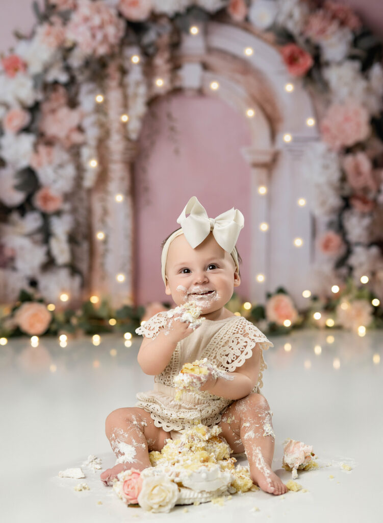 Baby girl eating cake on a floral arch backdrop. Photographed by Atlanta Cake Smash photographer. 