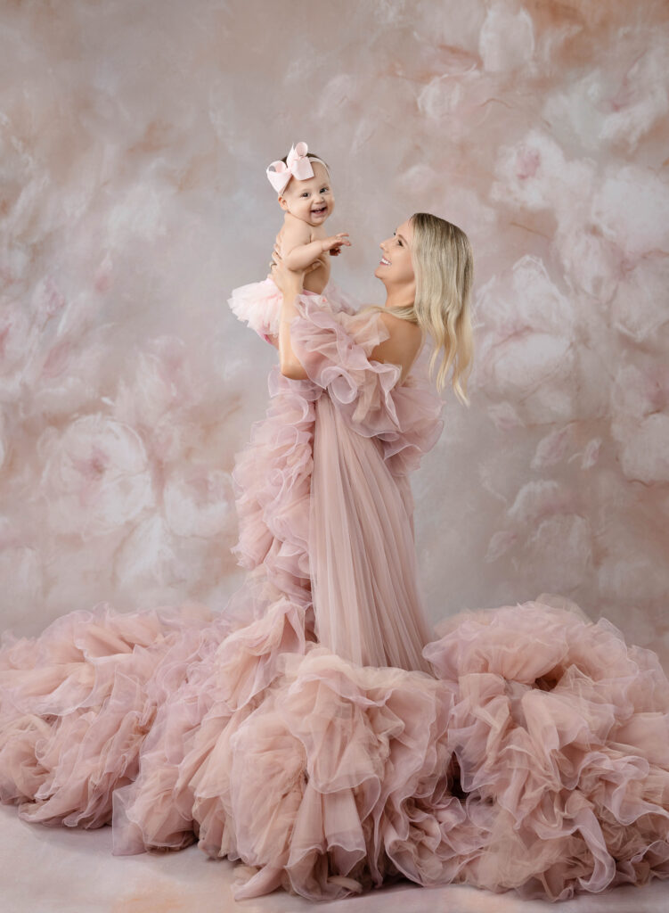Mom wearing pink gown and holding baby in air and smiling at her. Photographed by Atlanta Fine Art photographer.
