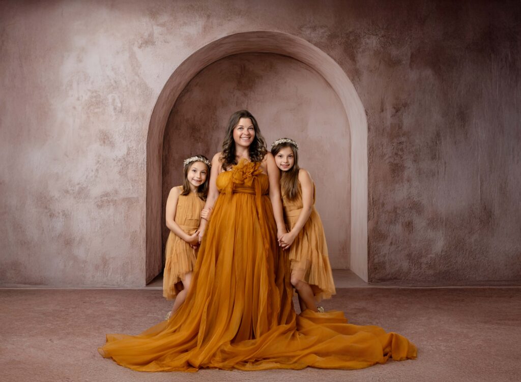 Mom and 2 girls in golden dresses taking a motherhood photo.