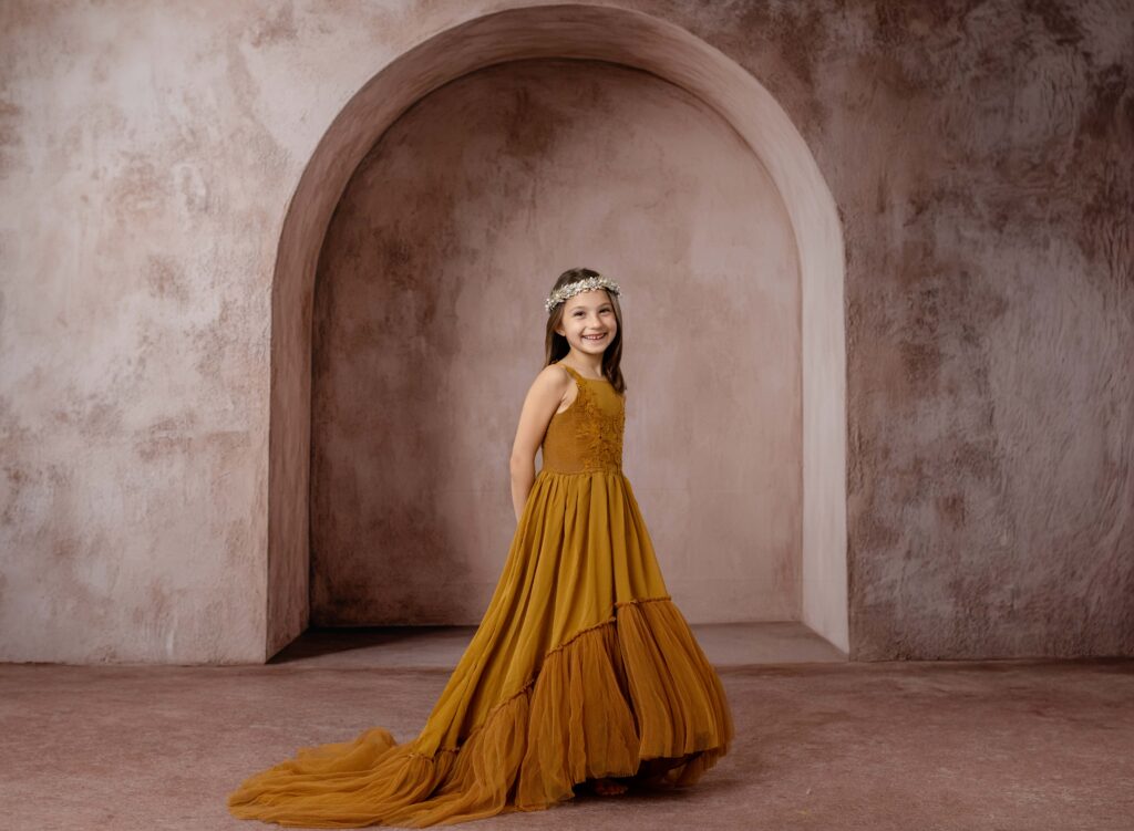7 year old girl standing with hands behind her back and smiling at camera for a professional studio portrait.