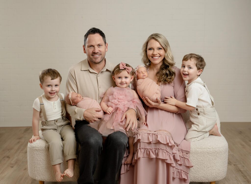Family of 7 with two sets of twins, posing on couch for family portrait.