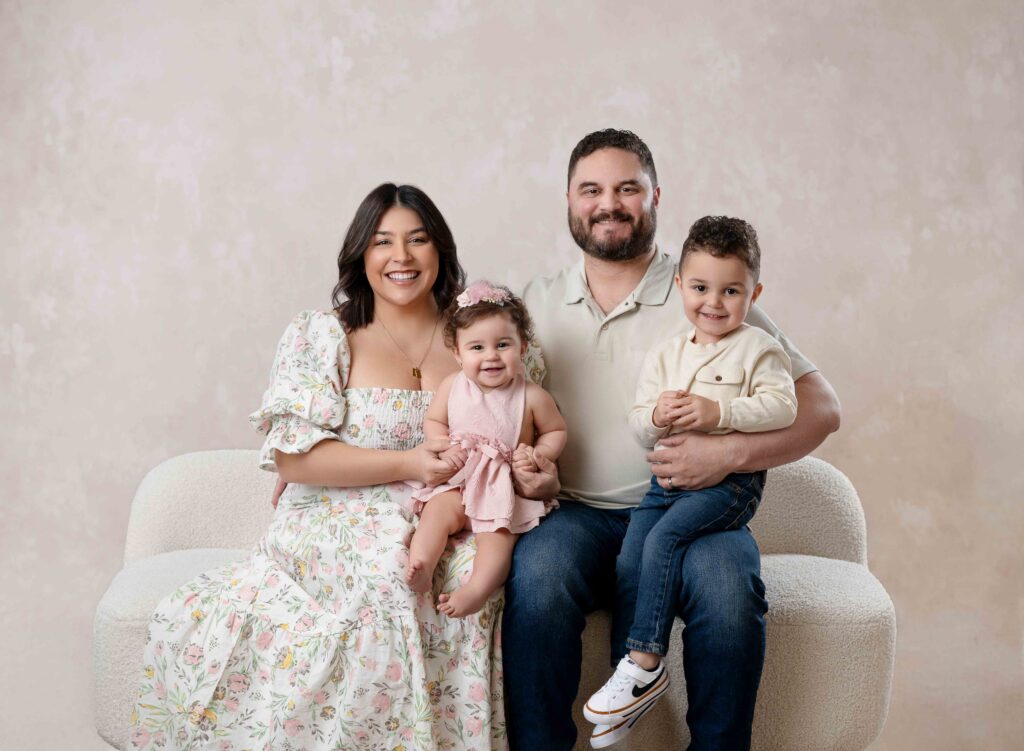Family of 4 sitting on couch and smiling at camera.