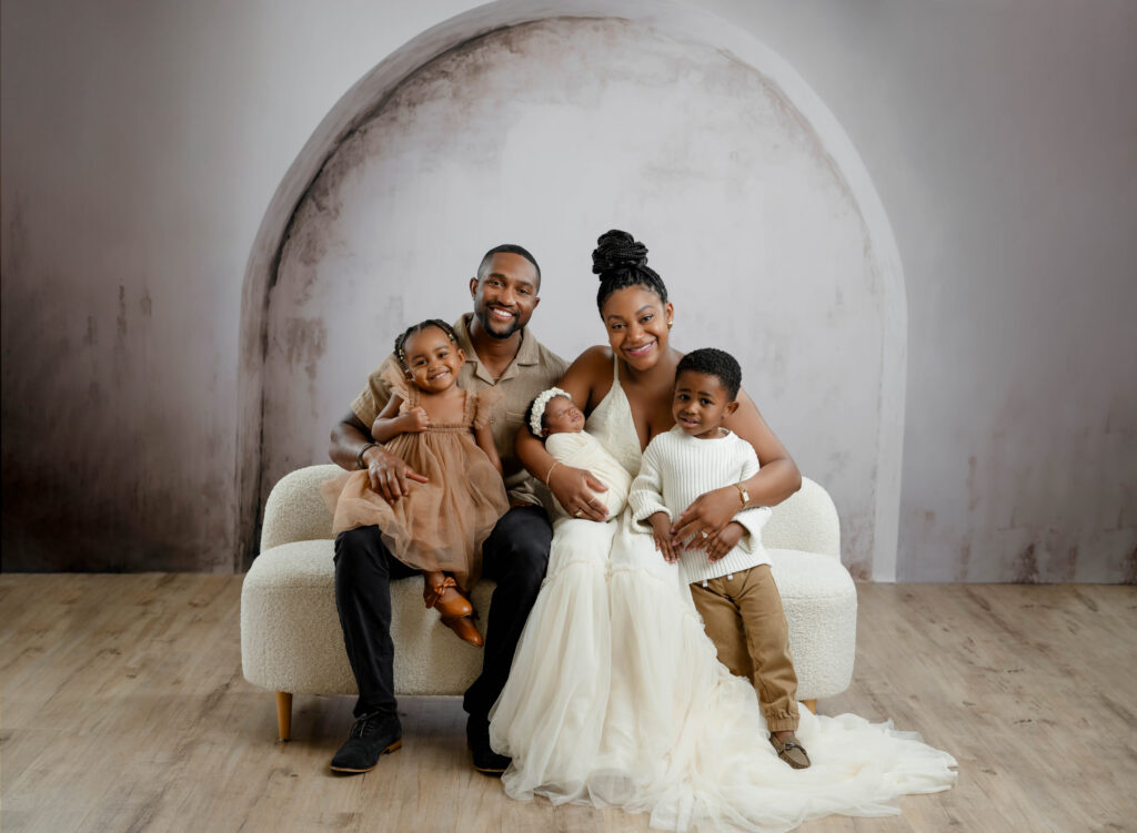 family of 5 sitting on white couch and smiling at the camera.