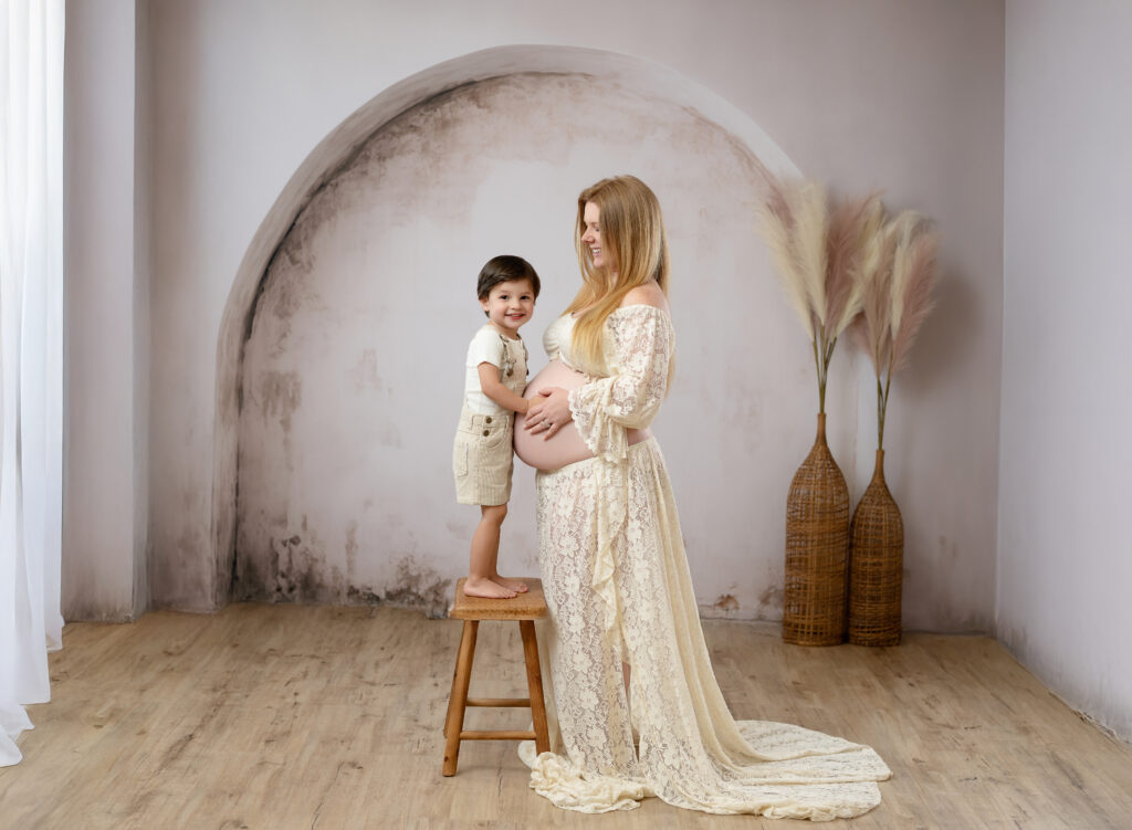 Pregnant woman in lace boho dress looking at her 3 year old son. 