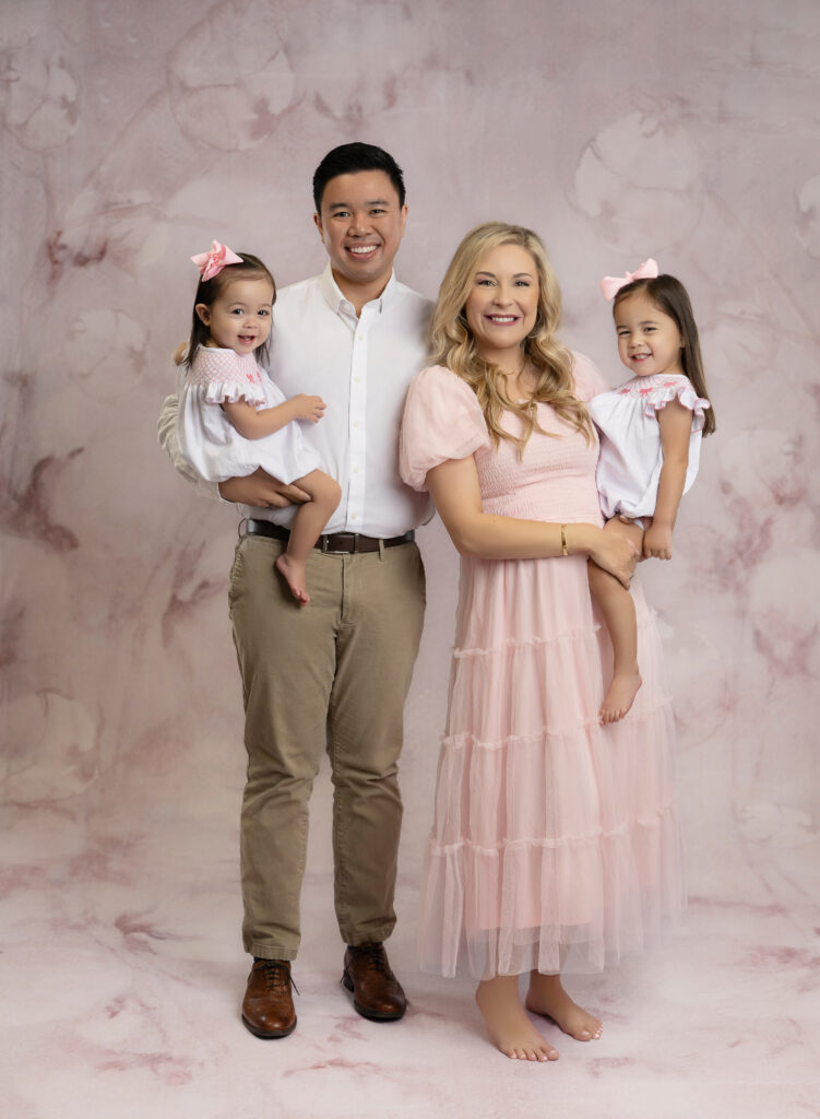 Family of 4 taking studio family photoshoot and dressed in pinsk and whites.