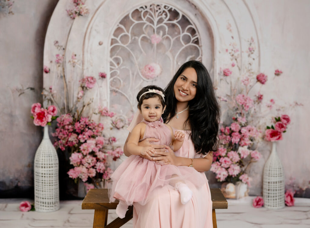 Mom and baby girl in pink taking photos in front of a spring door with pink flowers.