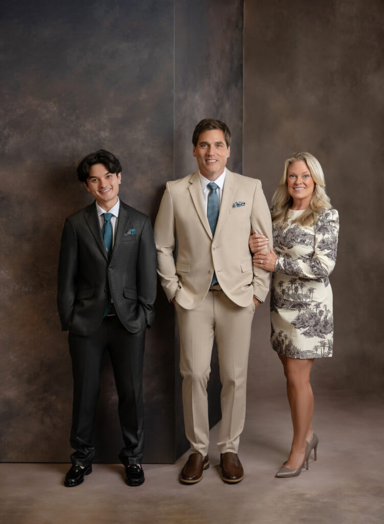 Mom, Dad and adult son photographing a family studio portrait on brown backdrop.