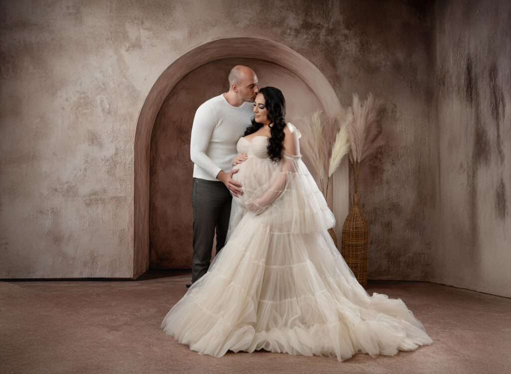 Husband kissing his pregnant wife and holding her belly.
