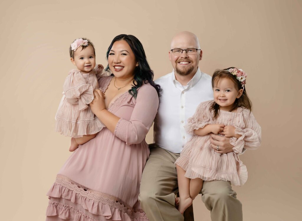 Mom and Dad sitting on bench and holding 2 kids, smiling at camera at Atlanta Family photo studio.