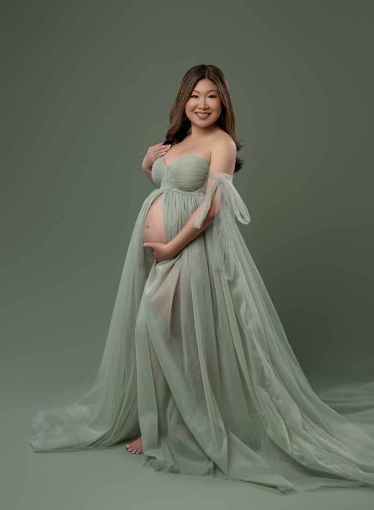 Women in mint green maternity dress, holding her baby bump and smiling at the camera.