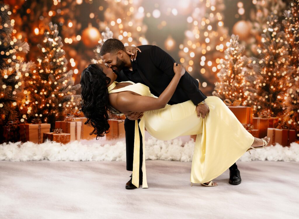 Man dipping women back on a christmas holiday backdrop set with golds and lights.