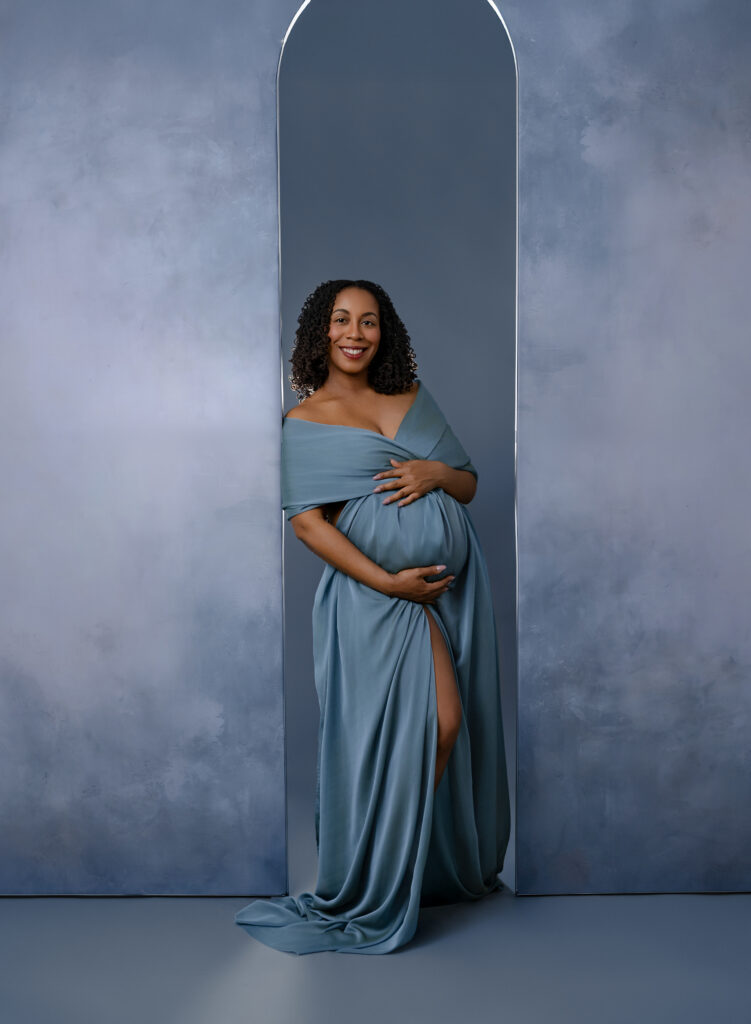 Mom draped in blue cloth leaning on blue arch backdrop. Atlanta Maternity Photography.