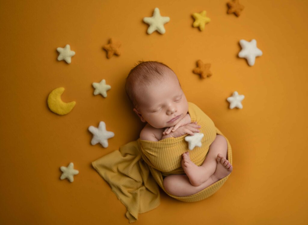 Newborn baby boy swaddled and surrounded by felted moon and stars