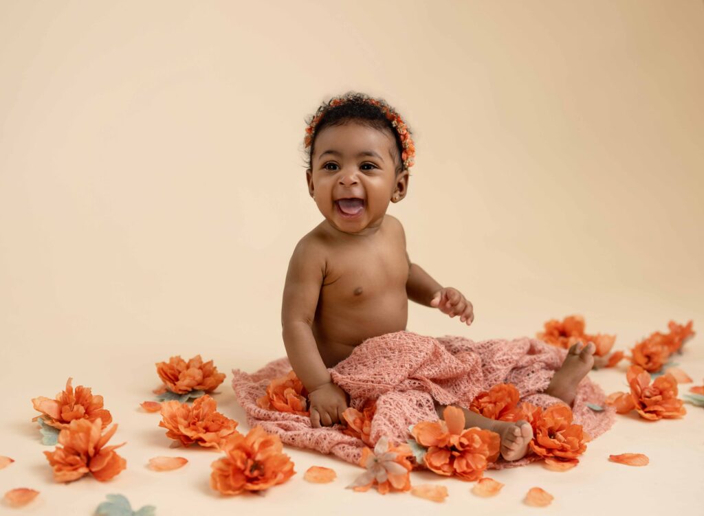 Baby sitting up in diaper cover and surrounded by peach florals and smiling.