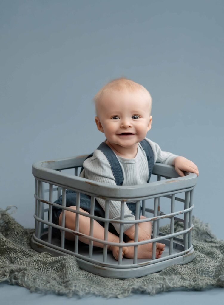 Baby boy sitting in a blue crate and smiling for his 6 month milestone photoshoot in Atlanta.