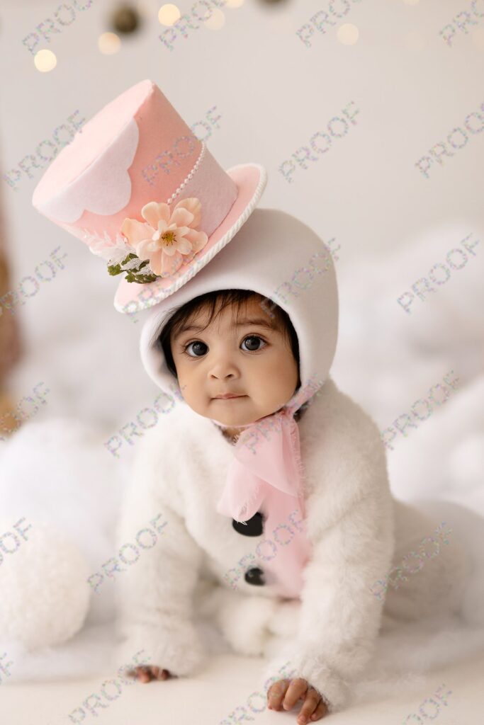 Baby girl in snowman suit with pink snowman hat.