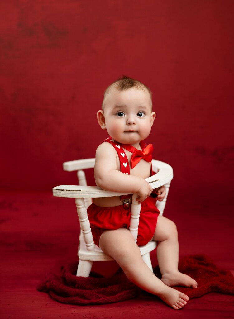 Baby in vday outfit and sitting in white wooden chair.
