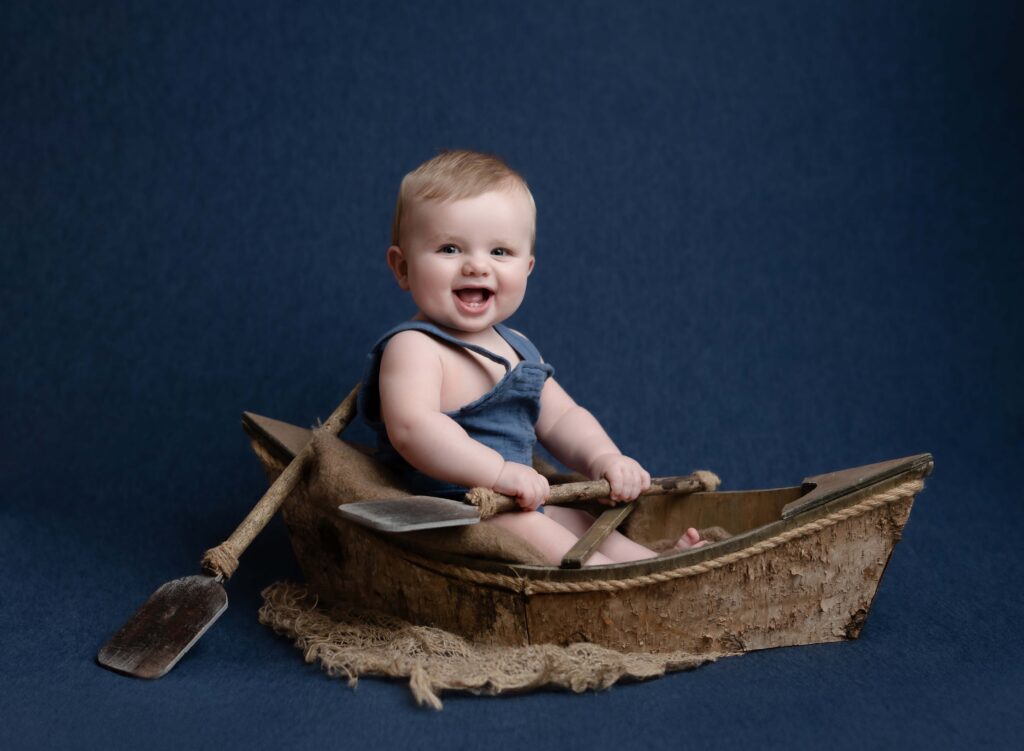 Baby sitting up in a wooden boat and smiling big.