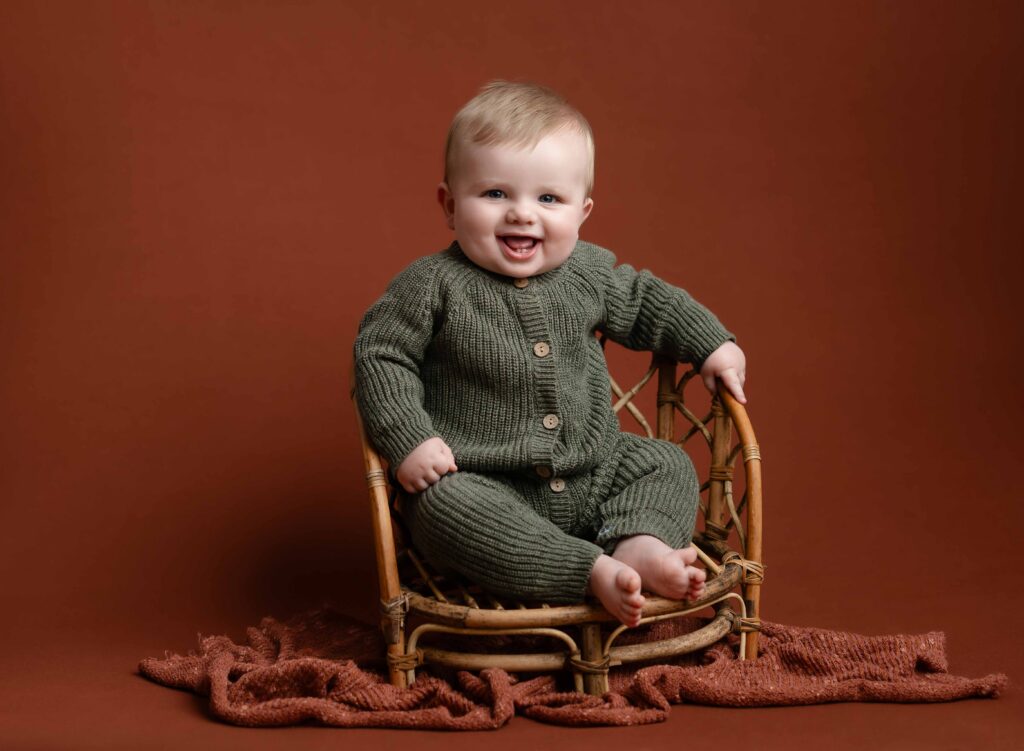 Baby sitting up in a bamboo chair and smiling.