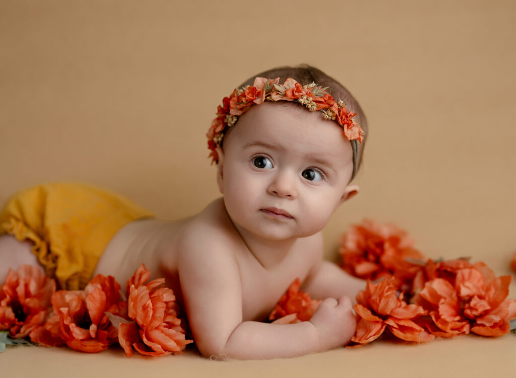 Baby girl laying on her tummy surround by peach coral flowers.
