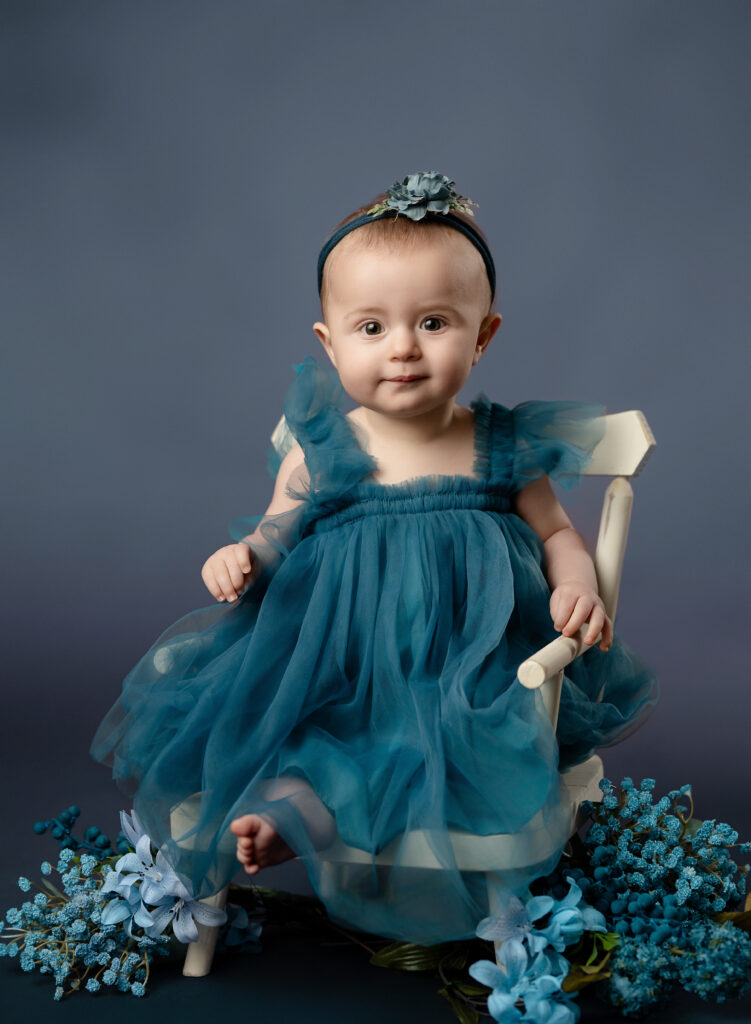 Baby girl sitting in tiny wooden chair and smiling.