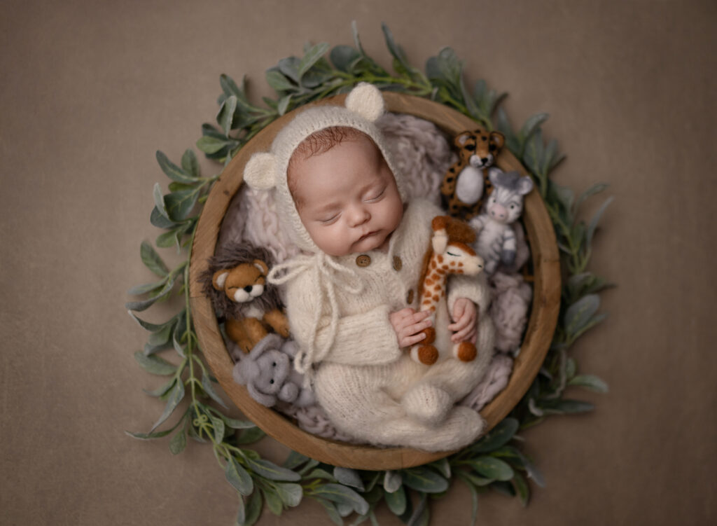 Baby boy sleeping in round bowl and snuggling with safari animals. 