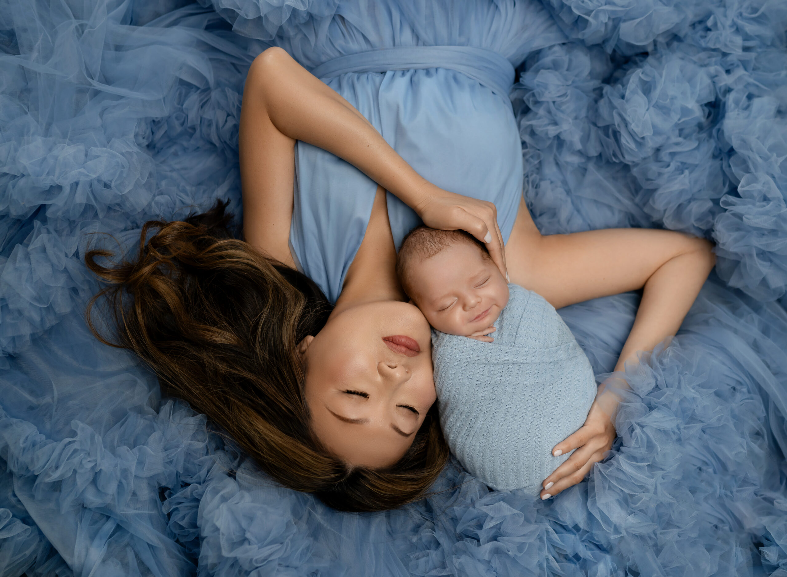 Mom in blue gown snuggling newborn baby boy.